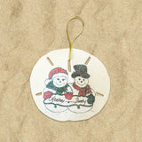 A round, beige sand dollar ornament with a Christmas theme, featuring illustrations of two snowmen with the names 'Heather' and 'Dusty' written on their hats.