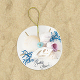 A round ornament with a sand dollar design, featuring shells in various shades of blue and white, and the text 'Nude Beach'.
