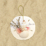 A round, beige holiday ornament featuring a shell cluster with greenery and the name 'Horide' printed on it.