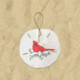 A round white ornament with a glittery red bird (cardinal) illustration, and twigs with snow, hanging by a golden loop.